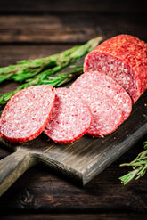 Pieces of salami sausage with rosemary on a cutting board.