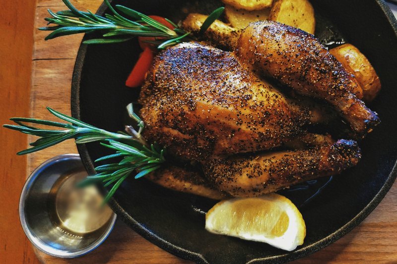 Whole roast chicken in a cast iron skillet with roasted potatoes, rosemary, and a lemon wedge