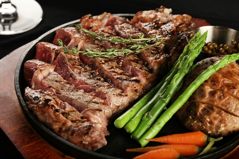Grilled steak sliced medium-rare on a cast iron platter with asparagus and carrots