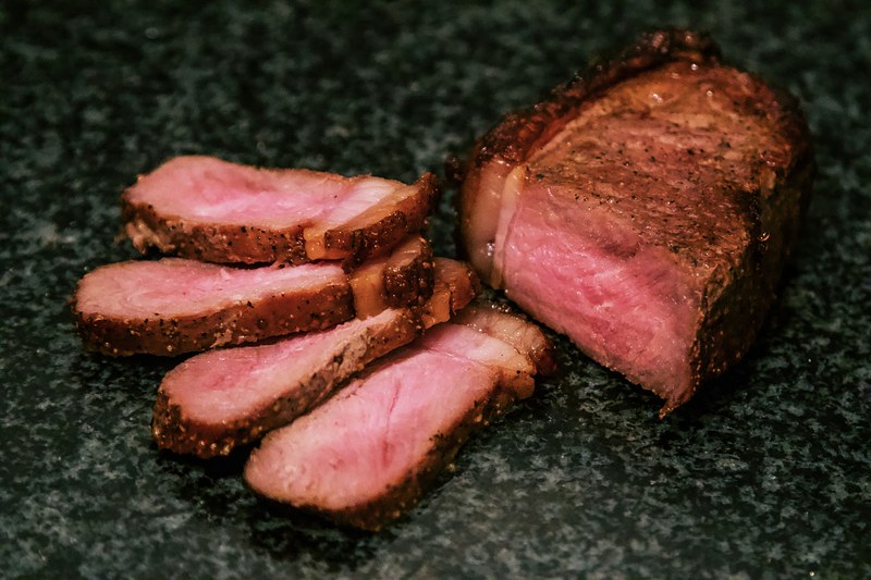 Seared lean roast sliced against the grain, rosy in the center, on a dark stone counter