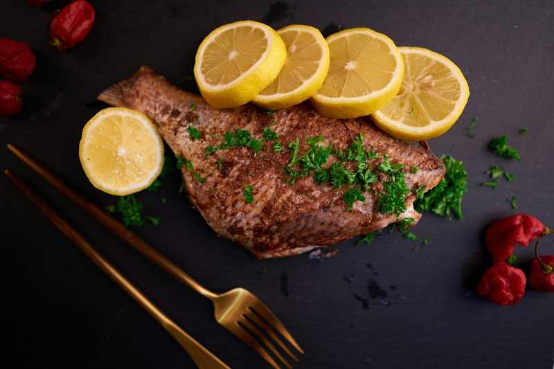 Pan-seared, spice-crusted fish with chopped parsley and lemon slices on a dark table