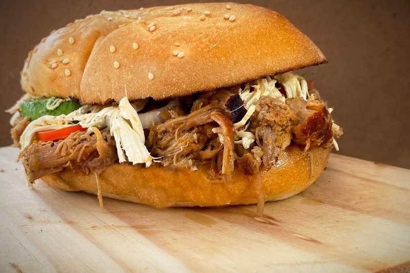 Pulled pork sandwich piled with slaw on a sesame seed bun on a wooden board
