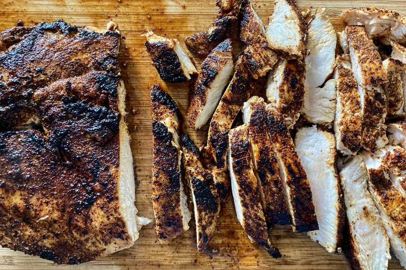 Grilled poultry with a dark seasoned crust, sliced on a wooden cutting board