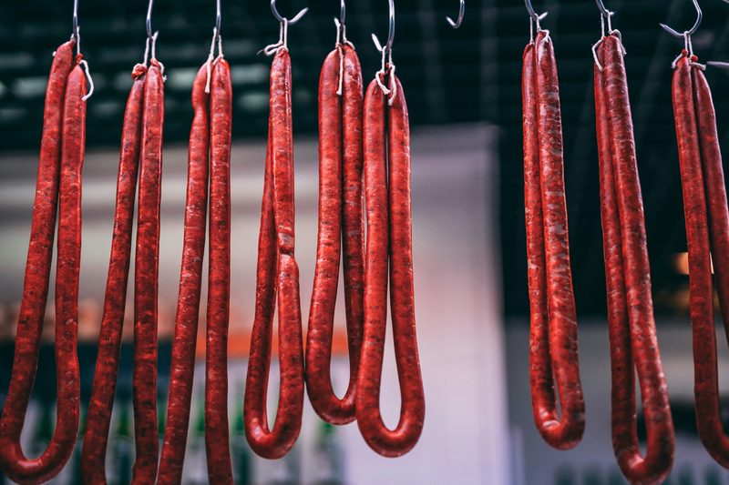 Long links of thin smoked sausage sticks hanging from hooks