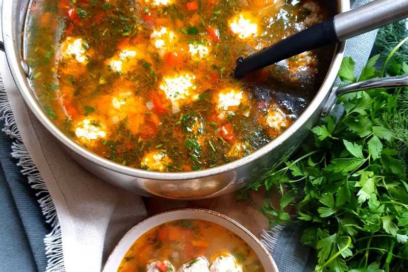 Meatball soup with vegetables in a steel pot, with a small bowl and fresh parsley