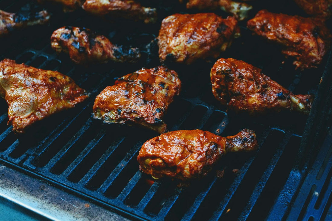 Glazed chicken drumsticks cooking on a black grill grate