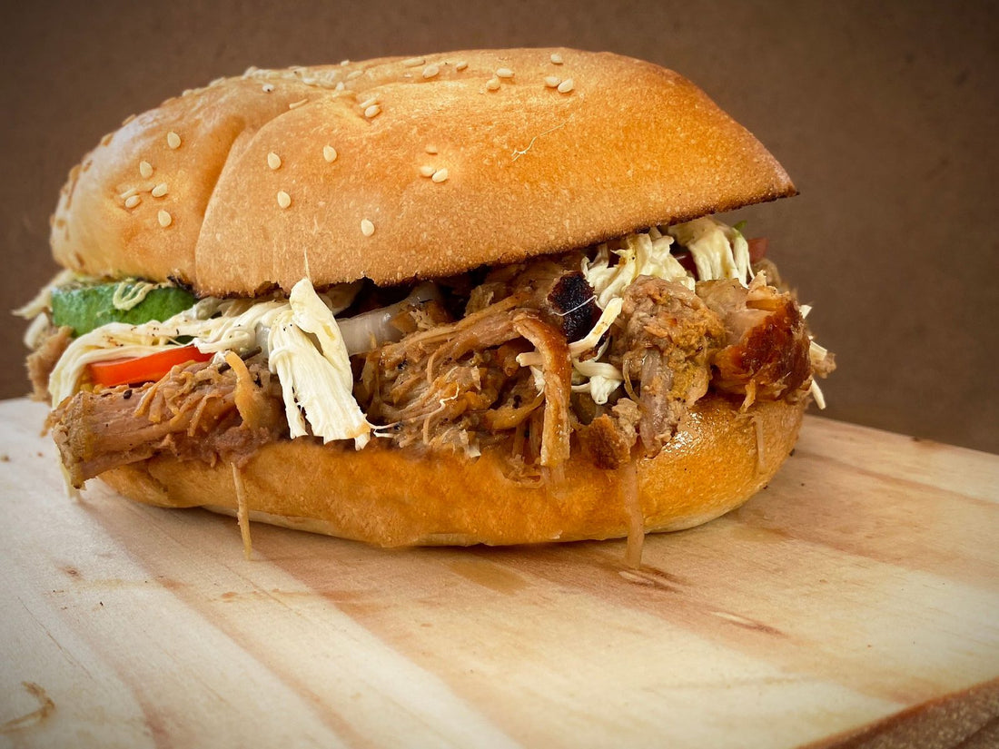 Pulled pork sandwich piled with slaw on a sesame seed bun on a wooden board