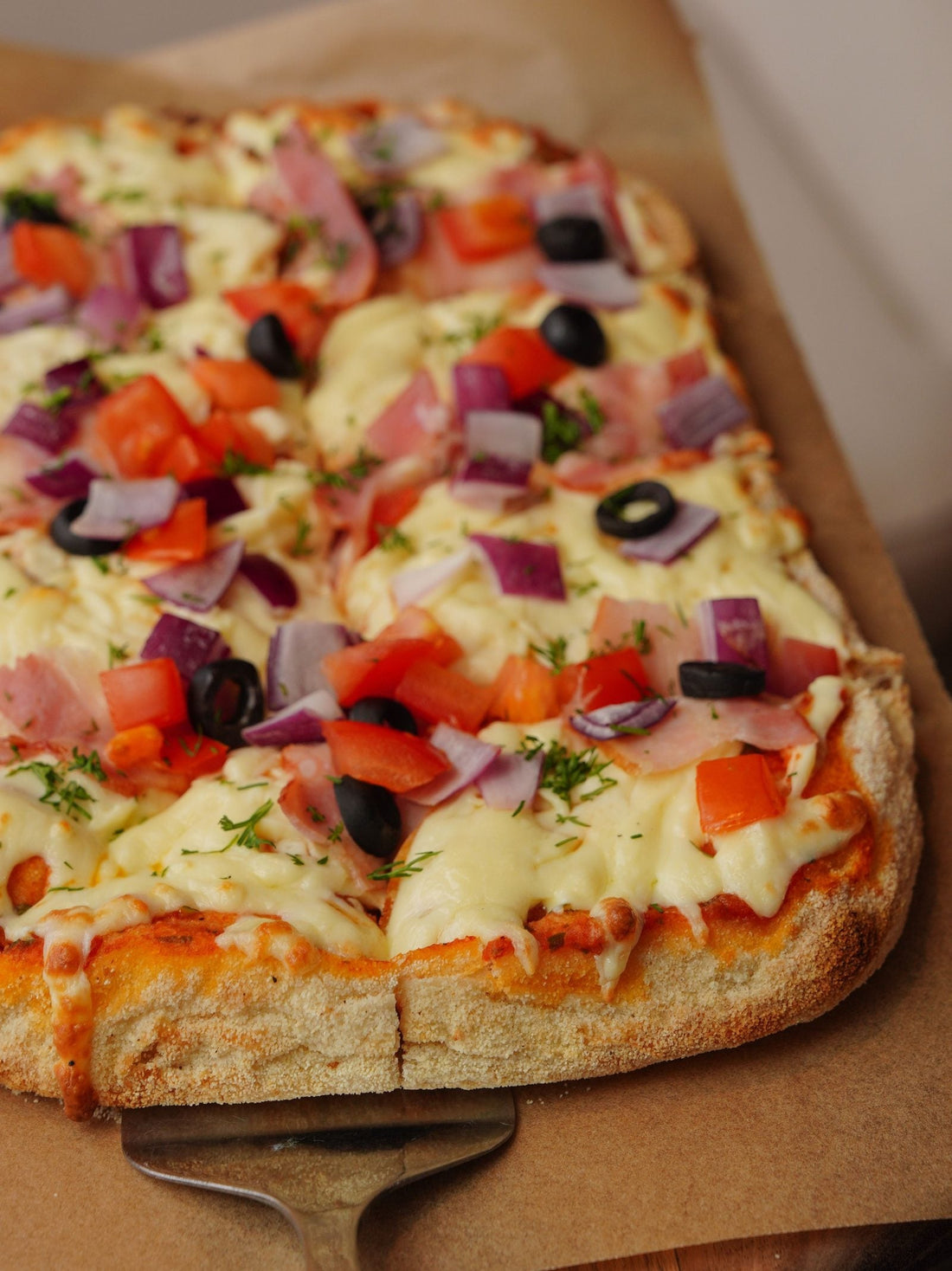 Rectangular sheet pan pizza topped with tomatoes, peppers, olives and red onion