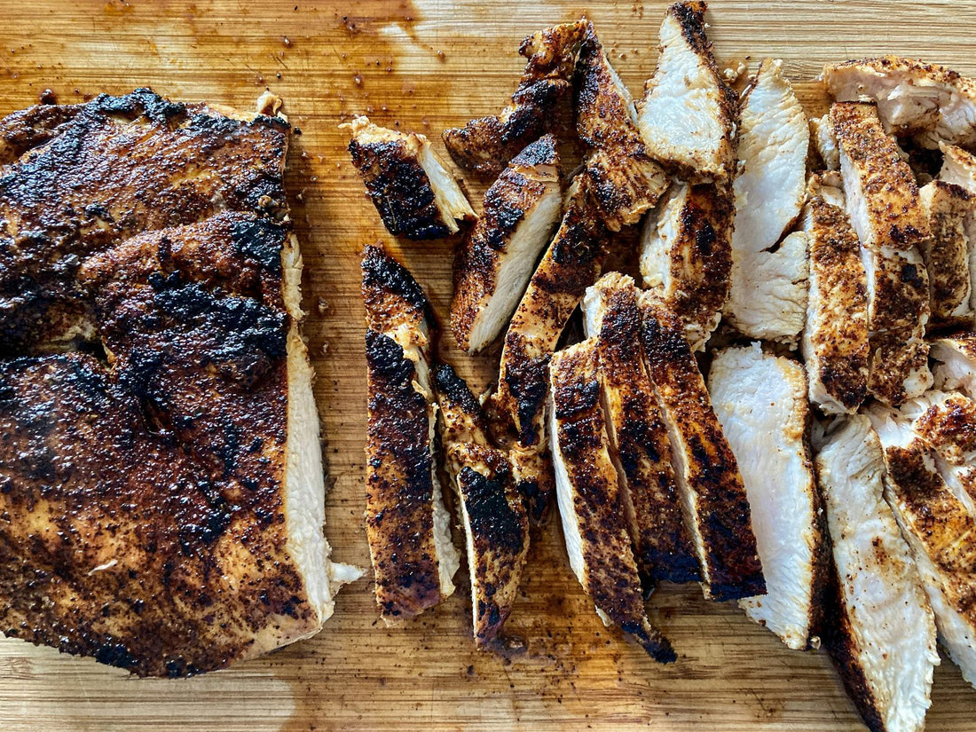 Grilled poultry with a dark seasoned crust, sliced on a wooden cutting board