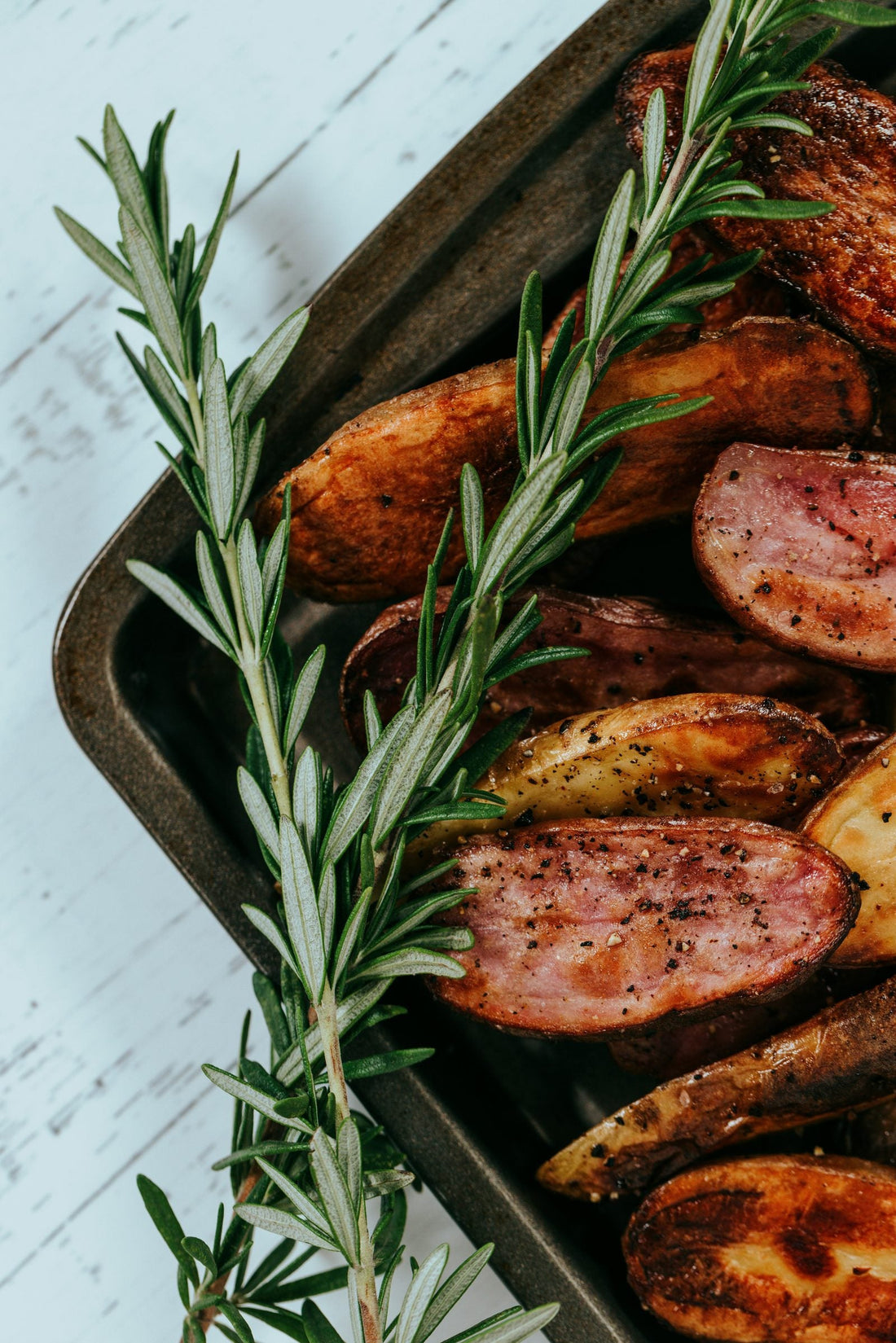 Roasted sausage slices and potato wedges with fresh rosemary in a dark sheet pan