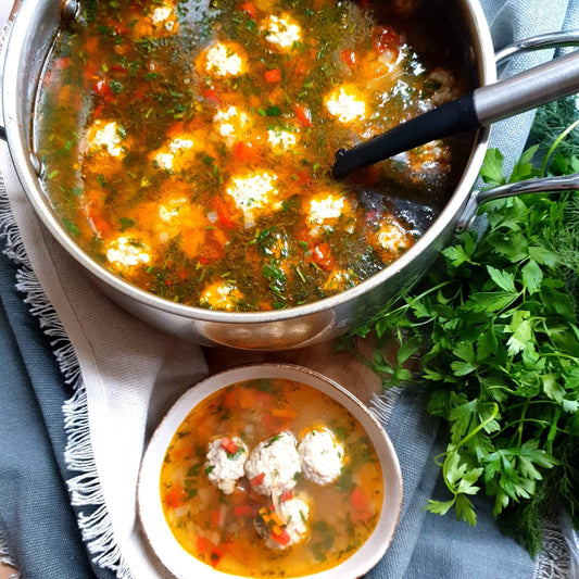 Meatball soup with vegetables in a steel pot, with a small bowl and fresh parsley