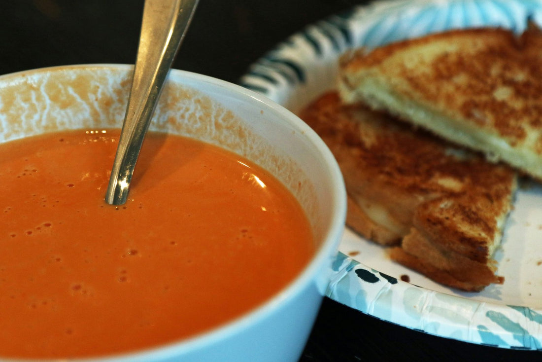Bowl of tomato soup with a spoon next to grilled cheese sandwich halves