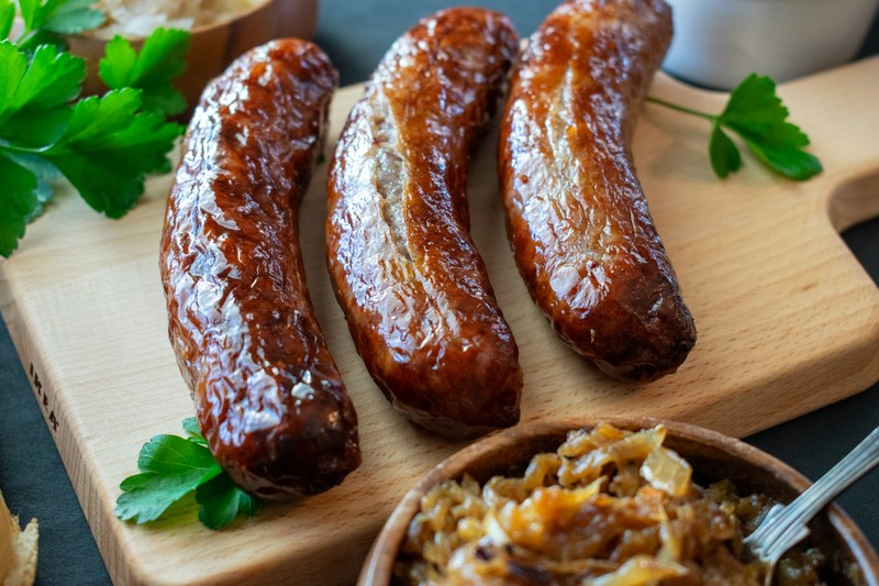 Browned bratwurst on a cutting board with a bowl of sauerkraut