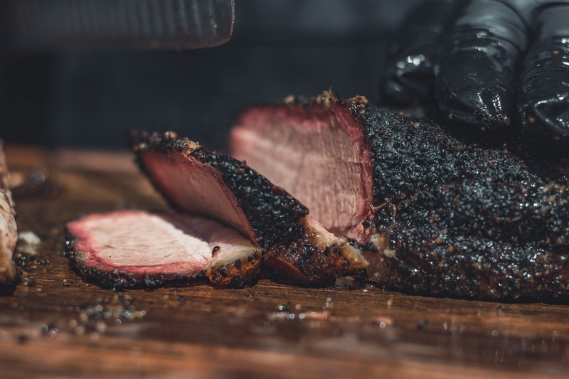 Smoked brisket sliced on a wooden board, showing the smoke ring and peppery bark