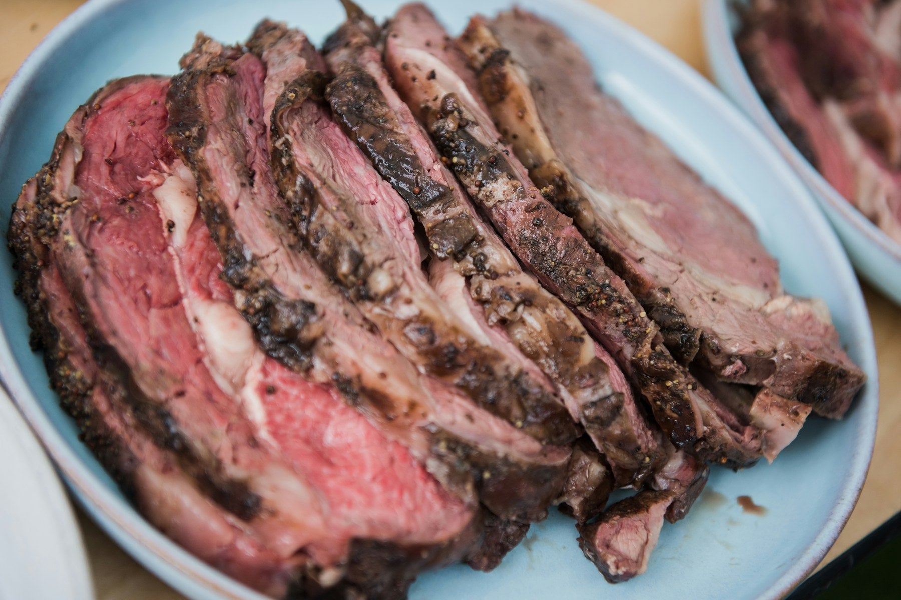 Bone-in prime rib sliced thick on a blue platter, rosy pink center with a dark seasoned crust