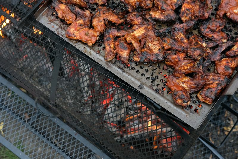 Chicken wings charring in a grill basket over hot coals