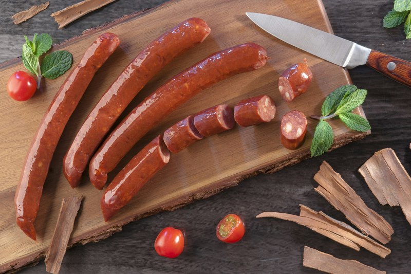 Smoked meat sticks on a wooden board with a knife