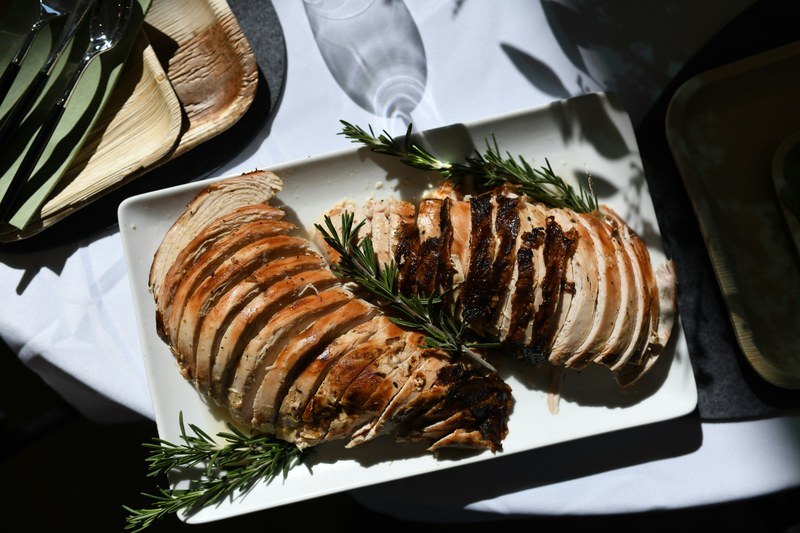 Sliced roast turkey breast with fresh rosemary on a white platter