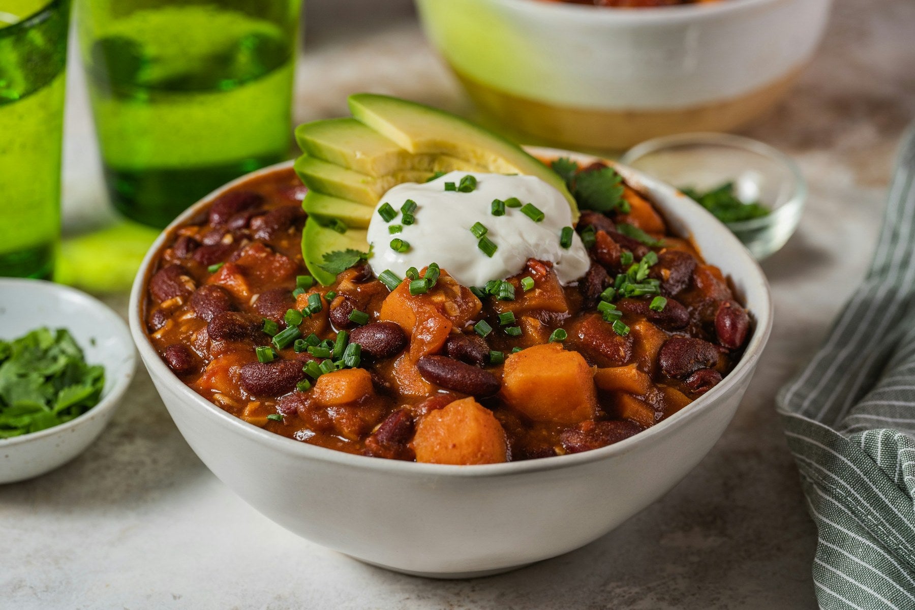 Bowl of bean and sweet potato chili topped with sour cream, green onion and avocado