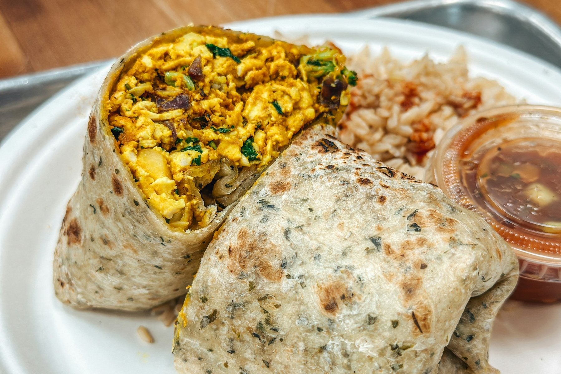 Breakfast burrito cut in half with rice and salsa on the side