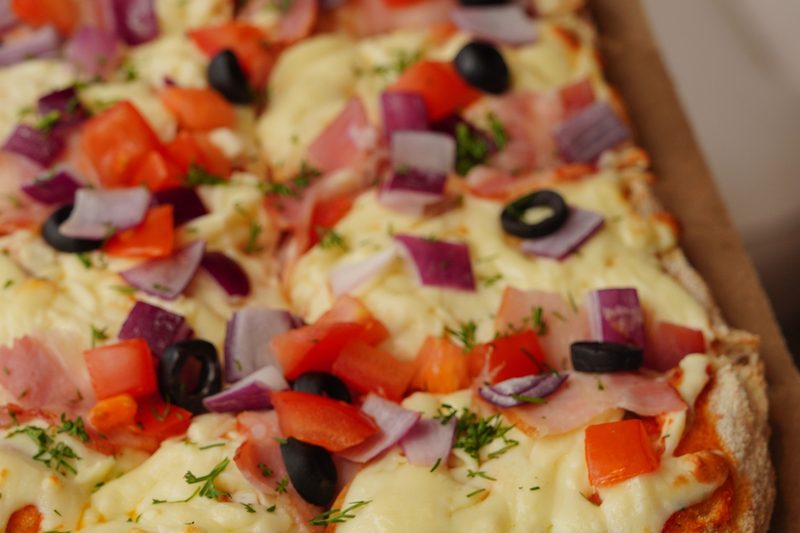 Rectangular sheet pan pizza topped with tomatoes, peppers, olives and red onion