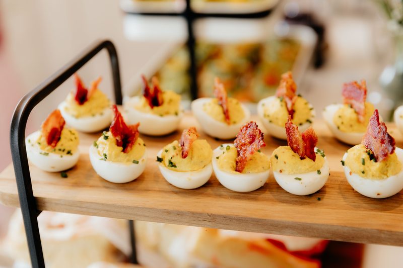 Deviled eggs topped with crispy bacon on a wooden serving tray