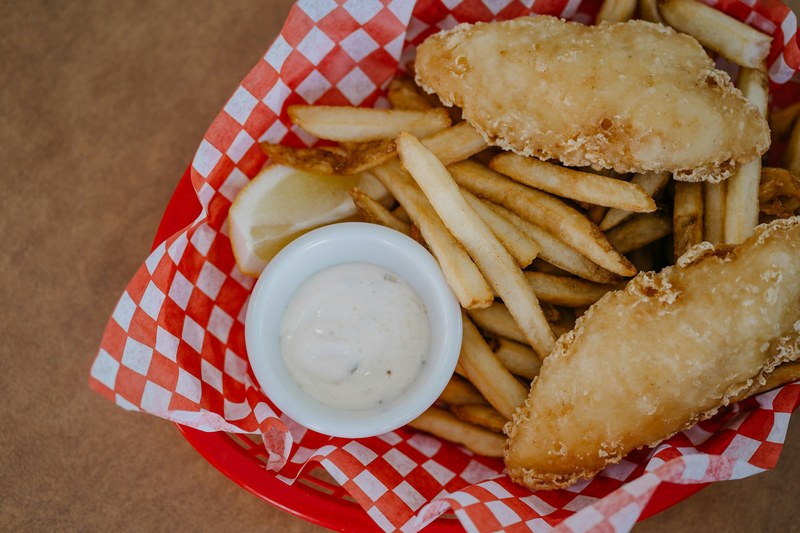 Crisp fried fish fillets with fries, lemon and tartar sauce in a checkered paper basket