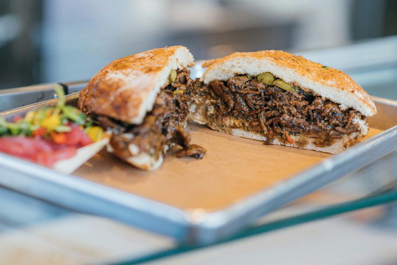 Beef sandwich on a crusty roll cut in half, packed with shredded beef and peppers