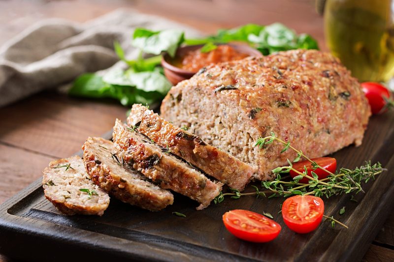 Sliced homemade meatloaf on a dark board with cherry tomatoes and fresh thyme