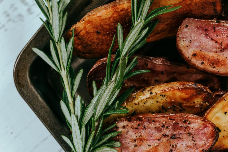 Roasted sausage slices and potato wedges with fresh rosemary in a dark sheet pan