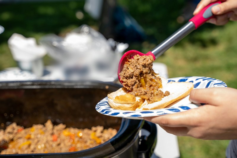 Sloppy joe filling spooned from a slow cooker onto a bun at a backyard cookout